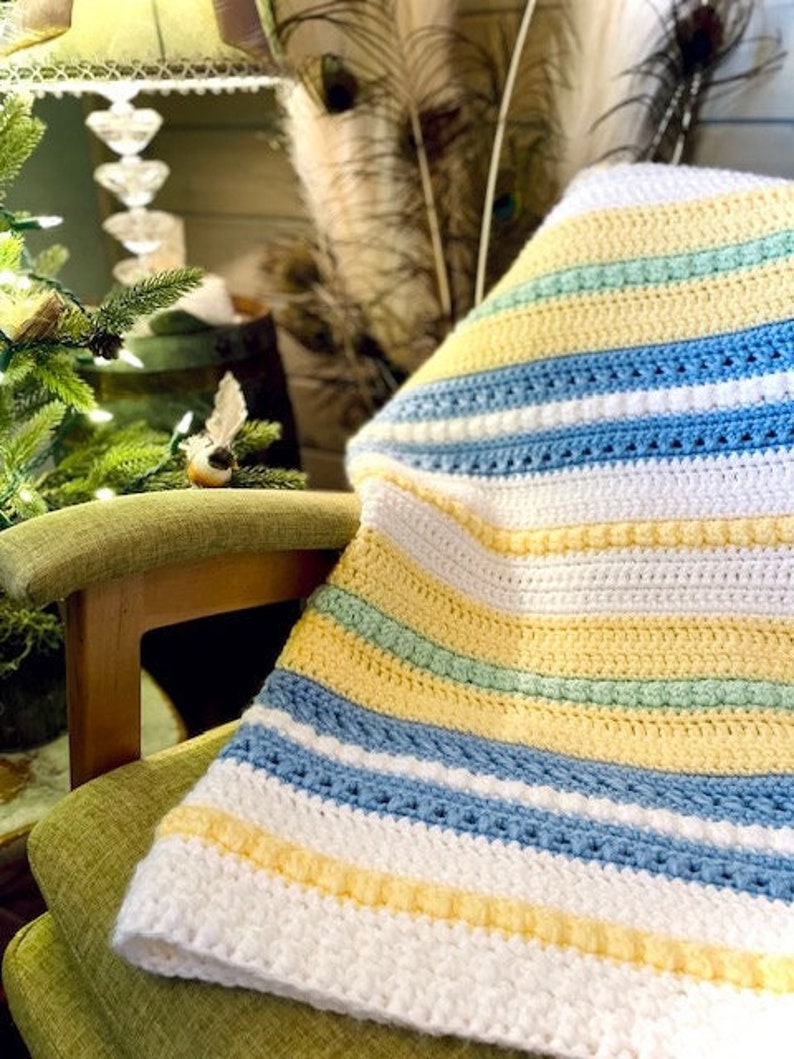 May include: A white, yellow, blue and green striped crocheted blanket draped over a wooden chair with a green cushion.