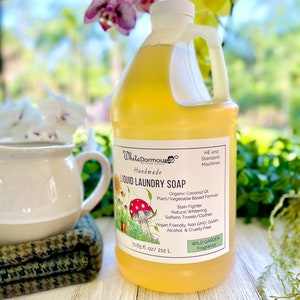 May include: A yellow plastic bottle of liquid laundry soap with a white label. The label says "White Dormous Artisan Soaps Handmade Liquid Laundry Soap" and lists the ingredients as "Organic Coconut Oil, Plant/Vegetable Based Formula, Stain Fighter, Natural Whitening, Softens Towels/Clothes, Vegan Friendly, Non GMO, Gluten, Alcohol & Cruelty Free". The label also says "Wild Garden Fragrance" and "71.65 fl oz/212 L".