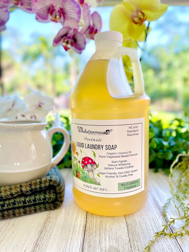 May include: A yellow plastic bottle of liquid laundry soap with a white label. The label says "White Dormous Artisan Soaps Handmade Liquid Laundry Soap" and lists the ingredients as "Organic Coconut Oil, Plant/Vegetable Based Formula, Stain Fighter, Natural Whitening, Softens Towels/Clothes, Vegan Friendly, Non GMO, Gluten, Alcohol & Cruelty Free". The label also says "Wild Garden Fragrance" and "71.65 fl oz/212 L".