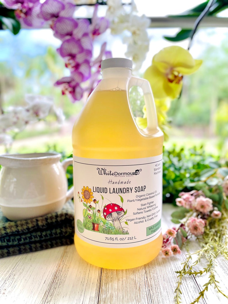 May include: A clear plastic bottle of liquid laundry soap with a white label. The label has a cartoon illustration of a mushroom and flowers. The text on the label reads "White Dormouse Artisan Soaps Handmade Liquid Laundry Soap Organic Coconut Oil Plant/Vegetable Based Formula Stain Fighter Natural Whitening Softens Towels/Clothes Vegan Friendly Non GMO Gluten Alcohol & Cruelty Free 71.65 fl. oz/ 212 L"