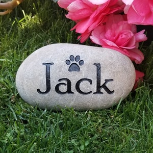 Peut inclure: Une pierre grise avec le nom "Jack" et une empreinte de patte noire gravée dessus. La pierre est posée sur un lit d'herbe verte.