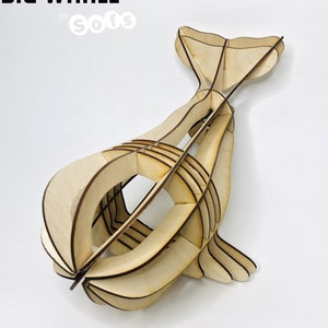 Könnte beinhalten: Ein 3D-Modell eines Wals aus Holz, montiert und bereit zur Präsentation. Das Modell besteht aus ineinandergreifenden Teilen und ist so konzipiert, dass es ohne Klebstoff oder Werkzeuge zusammengebaut werden kann. Das Modell ist mit "BIG WHALE" und "GROSSE BALEINE" beschriftet.