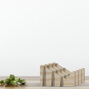 May include: A wooden desk organizer with a stepped design. The organizer is made of light-colored wood and has multiple slots for holding items. A small pile of green leaves sits to the left of the organizer on a wooden surface.