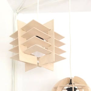 May include: Two wooden pendant lights, one with a geometric design and the other with a spherical design. Both lights are hanging from white cords.