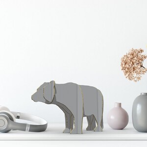 May include: A grey cardboard bear sculpture on a white surface with a pair of headphones, a book, and three vases with dried flowers.