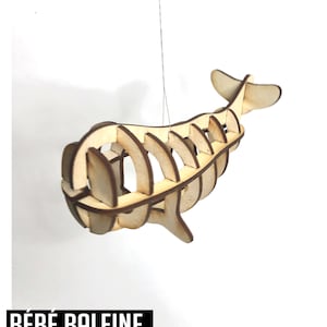 May include: A wooden 3D model of a baby whale, with the text "BABY WHALE" and "BÉBÉ BALEINE MODÈLE 3D ENCLENCHÉ" printed on the image. The model is hanging from a string.