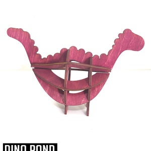 May include: A pink wooden dinosaur model with a rounded shape. The model is made of interlocking pieces and is labeled "ROUND DINO" and "DINO ROND MODELE 3D ENCLENCHÉ".