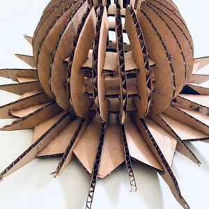 May include: A brown cardboard sculpture of a sphere with a starburst base. The sphere is made of many overlapping layers of cardboard, creating a geometric pattern.