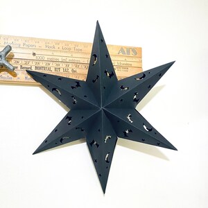 Peut inclure: Lanterne étoile en papier noir avec des découpes de chauves-souris, de lunes et d'étoiles. La lanterne est suspendue à un plafond blanc.