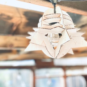 May include: A white cardboard lampshade with a geometric design. The lampshade is hanging from a ceiling and has a light bulb inside.