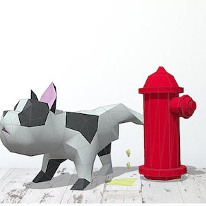 May include: A white and black paper model of a dog urinating on a red fire hydrant. The dog is made of paper and has a pink nose. The fire hydrant is also made of paper and has a black handle.