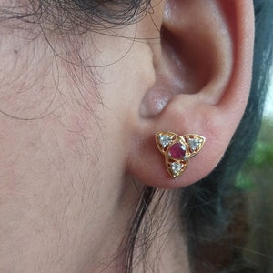 Op de afbeelding: Gouden oorbel met een rode edelsteen omringd door kleinere witte edelstenen.