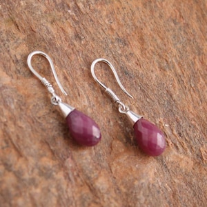 May include: A pair of silver dangle earrings with teardrop-shaped, faceted, deep purple gemstones.