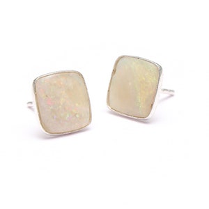 Pode incluir: Um par de brincos de prata com pedras de opala branca. As pedras são retangulares e têm um acabamento ligeiramente iridescente.