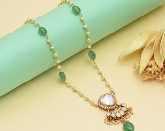 May include: Gold-toned necklace featuring a pendant with a large, clear stone and smaller white stones. The necklace has a delicate chain interspersed with small pearls and green gemstone beads. The pendant is teardrop-shaped, with a cluster of pearls and a green bead at the bottom.