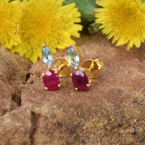 Pode incluir: Um par de brincos de ouro com uma pedra preciosa de rubi vermelho e uma pedra preciosa de topázio azul. Os brincos são engastados em uma moldura de ouro e têm um fecho de poste.