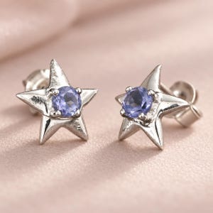 Peut inclure: Une paire de boucles d'oreilles à tige en forme d'étoiles à cinq branches. Chaque boucle d'oreille présente une pierre précieuse ronde et facettée bleu pervenche, sertie au centre de l'étoile, avec des fermoirs métalliques assortis.