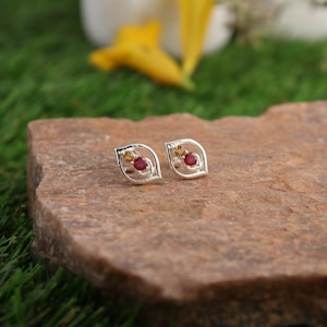 Pode incluir: Um par de brincos de prata com um design de folha. Cada brinco apresenta uma gema vermelha e amarela.