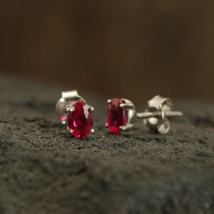 Pode incluir: Um par de brincos de prata com pedras preciosas vermelhas de forma oval.