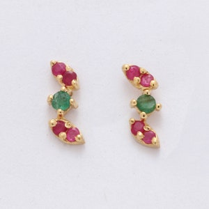 May include: A pair of gold earrings with a curved design featuring green and red gemstones.