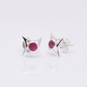 May include: A pair of silver earrings with a pink gemstone set in a geometric design.