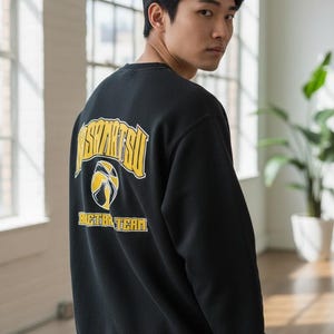 May include: Black crewneck sweatshirt with yellow and white text and a basketball graphic. The text on the back reads "KOSHIMATSU BASKETBALL TEAM". The sweatshirt is worn by a person.