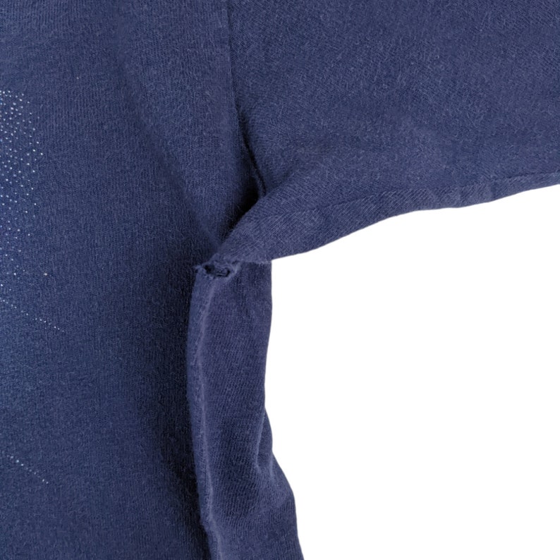 Peut inclure: Gros plan sur le tissu bleu marine d'un t-shirt, montrant les coutures et une petite d&eacute;chirure dans le tissu.