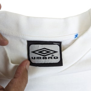 May include: White t-shirt with a black and gray Umbro logo label.