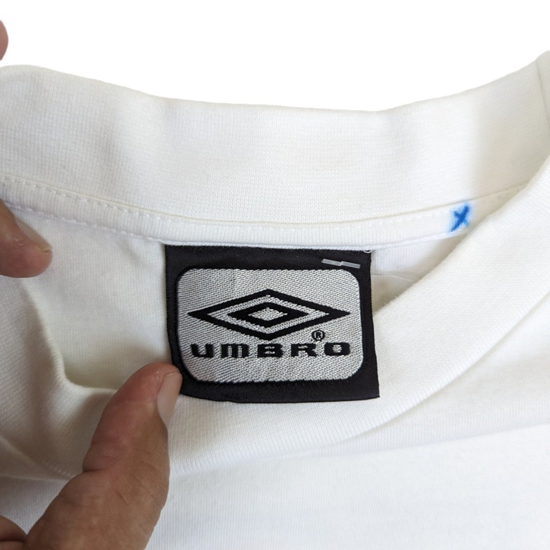 May include: White t-shirt with a black and gray Umbro logo label.