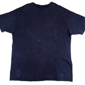 Peut inclure: Un t-shirt bleu fonc&eacute; &agrave; col rond et manches courtes. Le t-shirt est fait d'un tissu doux et confortable et a un aspect l&eacute;g&egrave;rement d&eacute;lav&eacute;.