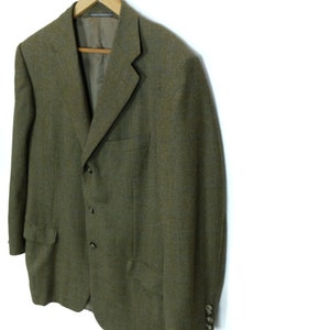 May include: A green tweed blazer with three buttons and a single button on each cuff. The blazer has a classic fit and a slightly textured fabric.