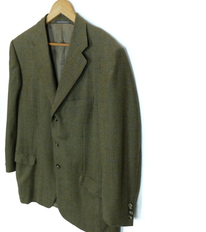 May include: A green tweed blazer with three buttons and a single button on each cuff. The blazer has a classic fit and a slightly textured fabric.