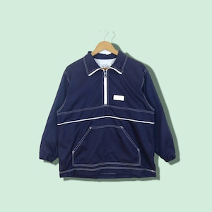 May include: A navy blue windbreaker jacket with white stitching and a white zipper. The jacket has a small white patch on the chest with the word "OG" on it.
