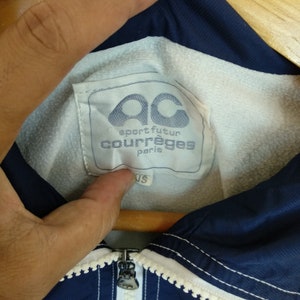 May include: A navy blue jacket with white piping and a white label that says "sport futur courr&egrave;ges paris".