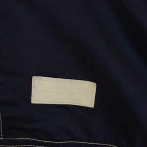 May include: A white label with the text "Courr&egrave;ges Sport futur" on a dark blue fabric background.