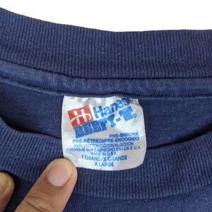 Peut inclure: Une &eacute;tiquette de t-shirt bleu Hanes Beefy-T avec du texte blanc. L'&eacute;tiquette indique "Pr&eacute;-r&eacute;tr&eacute;ci", "100% coton", "Fabriqu&eacute; aux &Eacute;tats-Unis", "T Grand/X Grande" et "X Large".