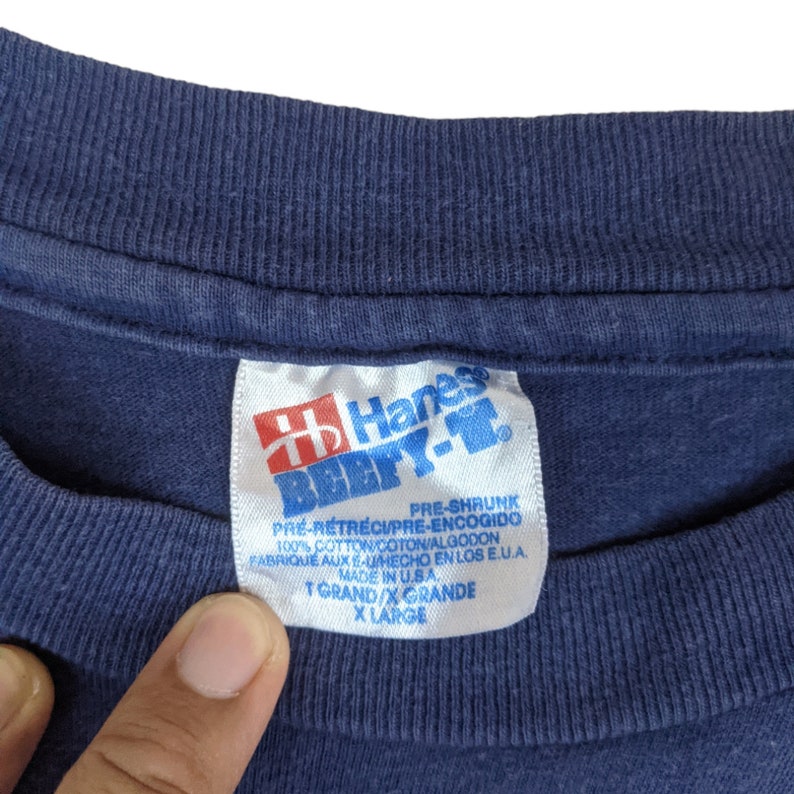 Peut inclure: Une &eacute;tiquette de t-shirt bleu Hanes Beefy-T avec du texte blanc. L'&eacute;tiquette indique "Pr&eacute;-r&eacute;tr&eacute;ci", "100% coton", "Fabriqu&eacute; aux &Eacute;tats-Unis", "T Grand/X Grande" et "X Large".