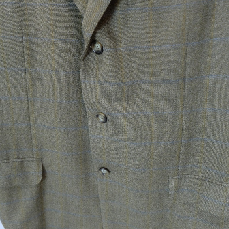 May include: A brown blazer with a subtle blue and yellow plaid pattern. The blazer has four buttons down the front.