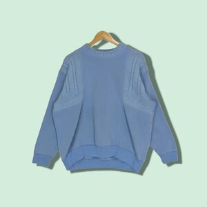 May include: A light blue jumper with a cable knit design on the shoulders. The jumper has a crew neck and long sleeves.