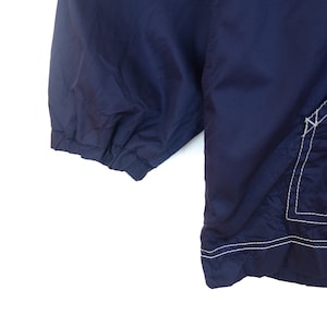 May include: A navy blue jacket with white stitching detail. The jacket has a zipper closure and a drawstring hood.