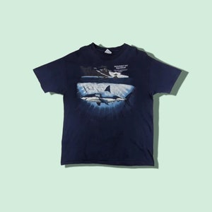 Peut inclure: Un t-shirt bleu marine avec un graphique d'un grand requin blanc nageant dans l'oc&eacute;an. Le texte "Monterey Bay Aquarium" est imprim&eacute; sur le t-shirt.