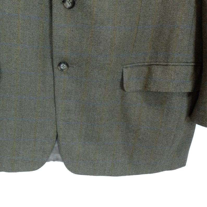 May include: A brown blazer with a subtle blue and brown plaid pattern. The blazer has two button closures and a flap pocket on the right side.