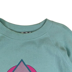 Puede incluir: Una sudadera azul claro con un dise&ntilde;o geom&eacute;trico rosa y turquesa en la parte delantera.