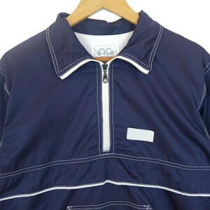 May include: A navy blue windbreaker jacket with white stitching and a zipper closure. The jacket has a small logo on the chest that says "AC".