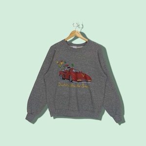 May include: A gray sweatshirt with a red car and a figure driving it. The car has a Christmas tree and presents on top. The text "Dashing thru the Snow" is printed below the car.