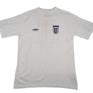 May include: White t-shirt with a red and blue England crest and a small, black and white logo of a diamond shape with the text "umbro" above it.