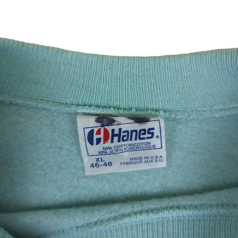 Puede incluir: Una sudadera Hanes azul claro con una etiqueta blanca que dice "Hanes" en letras azules. La etiqueta tambi&eacute;n dice "50% Algod&oacute;n/Coton 50% Acr&iacute;lico/Acrylique" y "XL 46-48" en letras negras. La etiqueta tambi&eacute;n dice "Made in U.S.A. Fabrique aux E.U." en letras negras.
