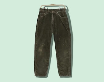 May include: Olive green corduroy pants hanging on a gold-colored hanger. The pants have a classic five-pocket design and a button and zipper closure. The corduroy fabric has a textured appearance, and there are some worn spots on the front of the pants.