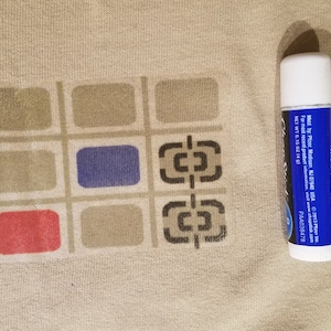 May include: A beige fabric with a colorful geometric pattern and a lip balm. The pattern features squares in red, blue, and gray. The lip balm is white and blue with text that reads "MOISTURIZER".