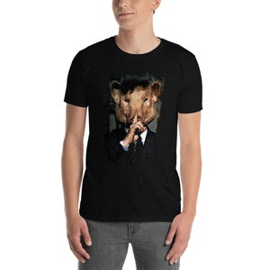 May include: Black t-shirt featuring a surreal image of a person wearing a pig mask, dressed in a suit, with a finger over their lips. The graphic has a vintage, distressed look. The t-shirt is made of a soft, comfortable material.